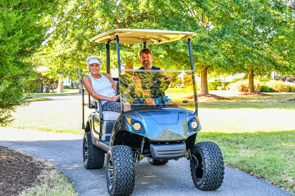 A smiling couple riding in a golf cart along a tree-lined path